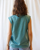 Person wearing a teal sleeveless top against a white curtain background