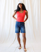 Woman wearing a red tank top and blue shorts against a white curtain background