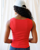 Person wearing a red tank top and white cap from behind, standing against a plain background