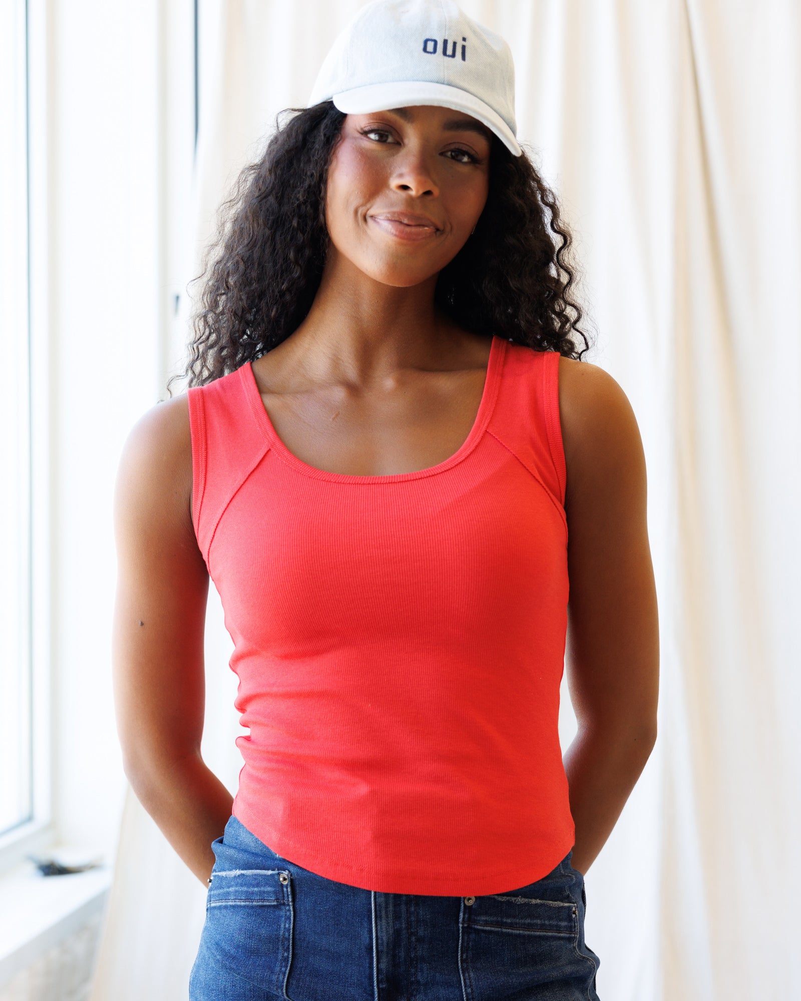 Woman wearing a red tank top and white cap with 'oui' logo indoors.