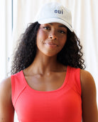 Image of a woman wearing a light wash denim hat with "OUI" embroidered in navy thread and wearing a red tank top