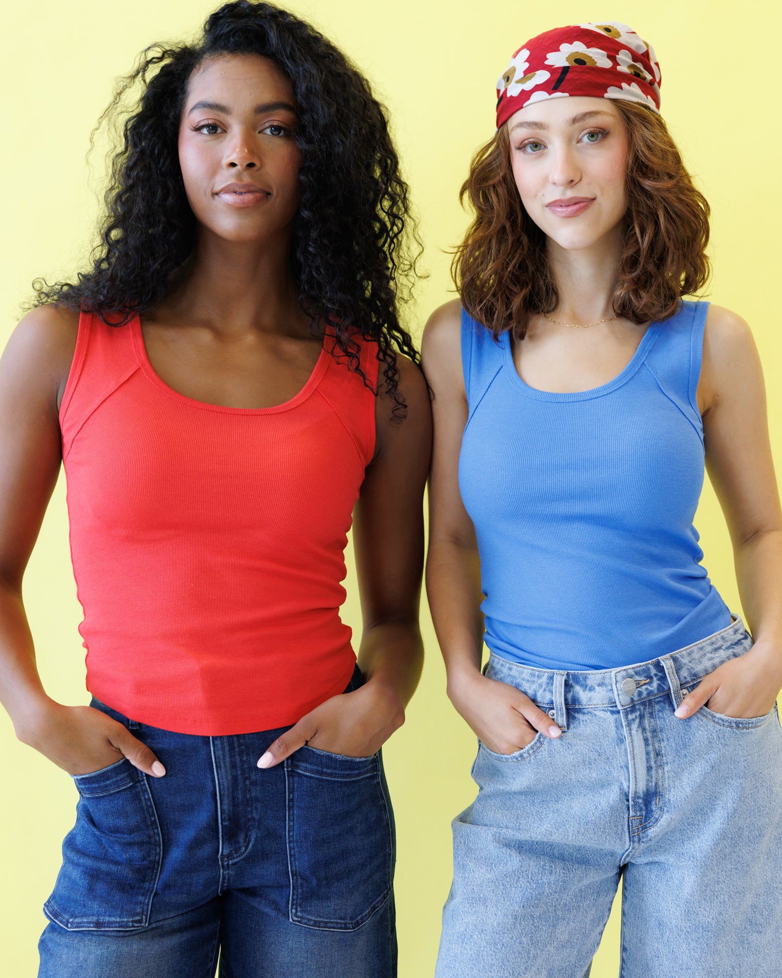 Two women wearing tank tops and jeans against a yellow background