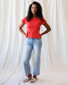Woman wearing a red top and light blue jeans against a plain background