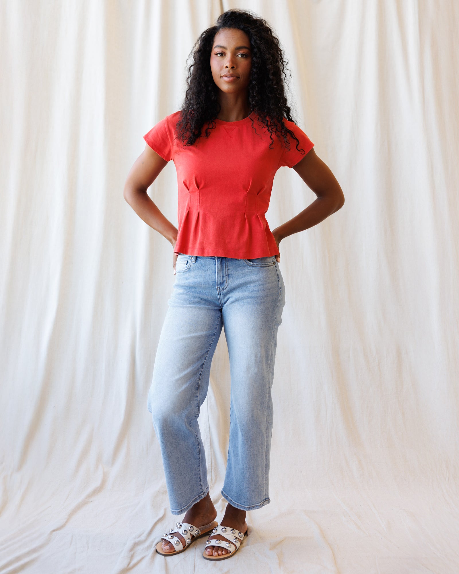 Woman wearing a red top and light blue jeans against a plain background