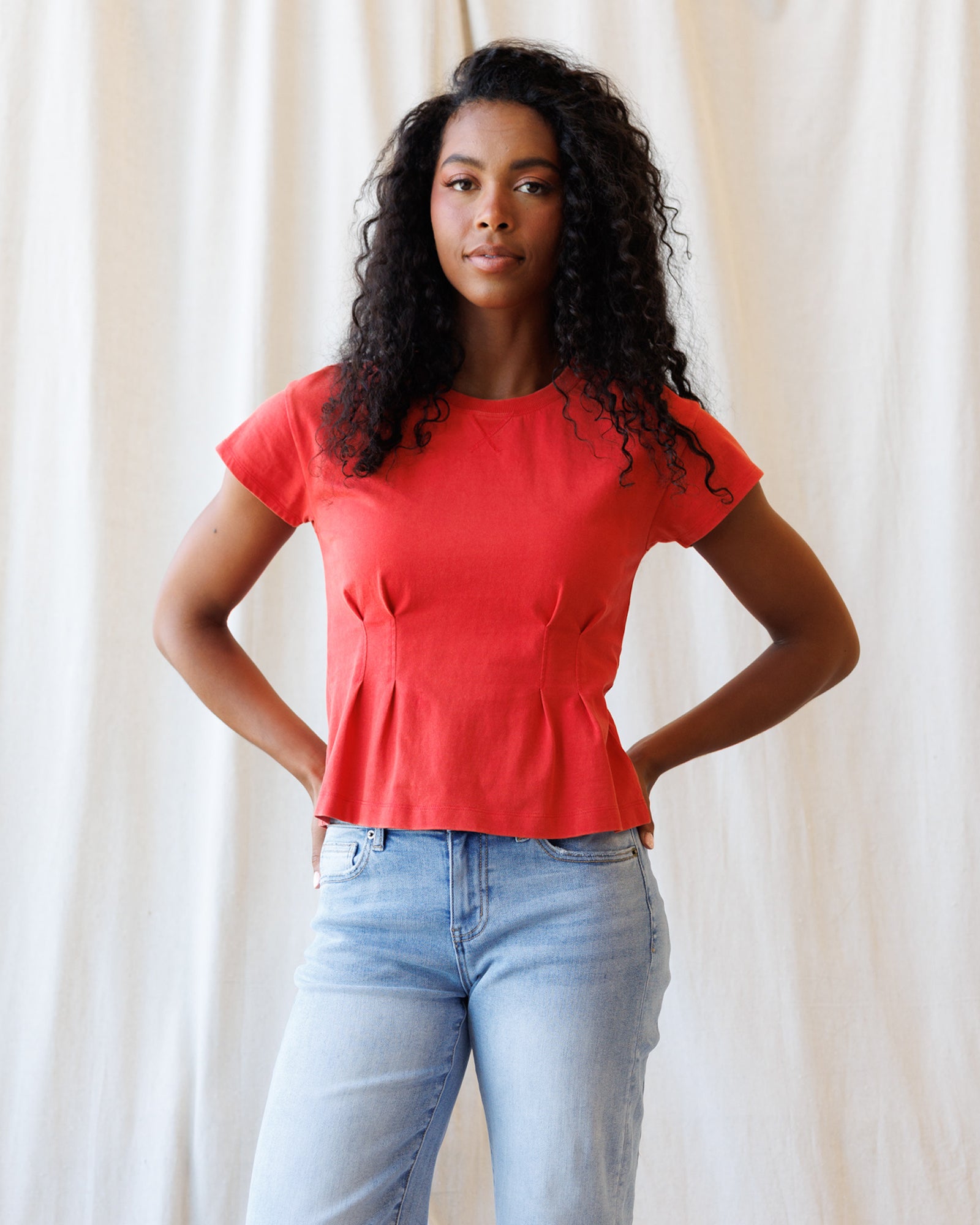 Woman wearing a red top and light blue jeans against a plain background
