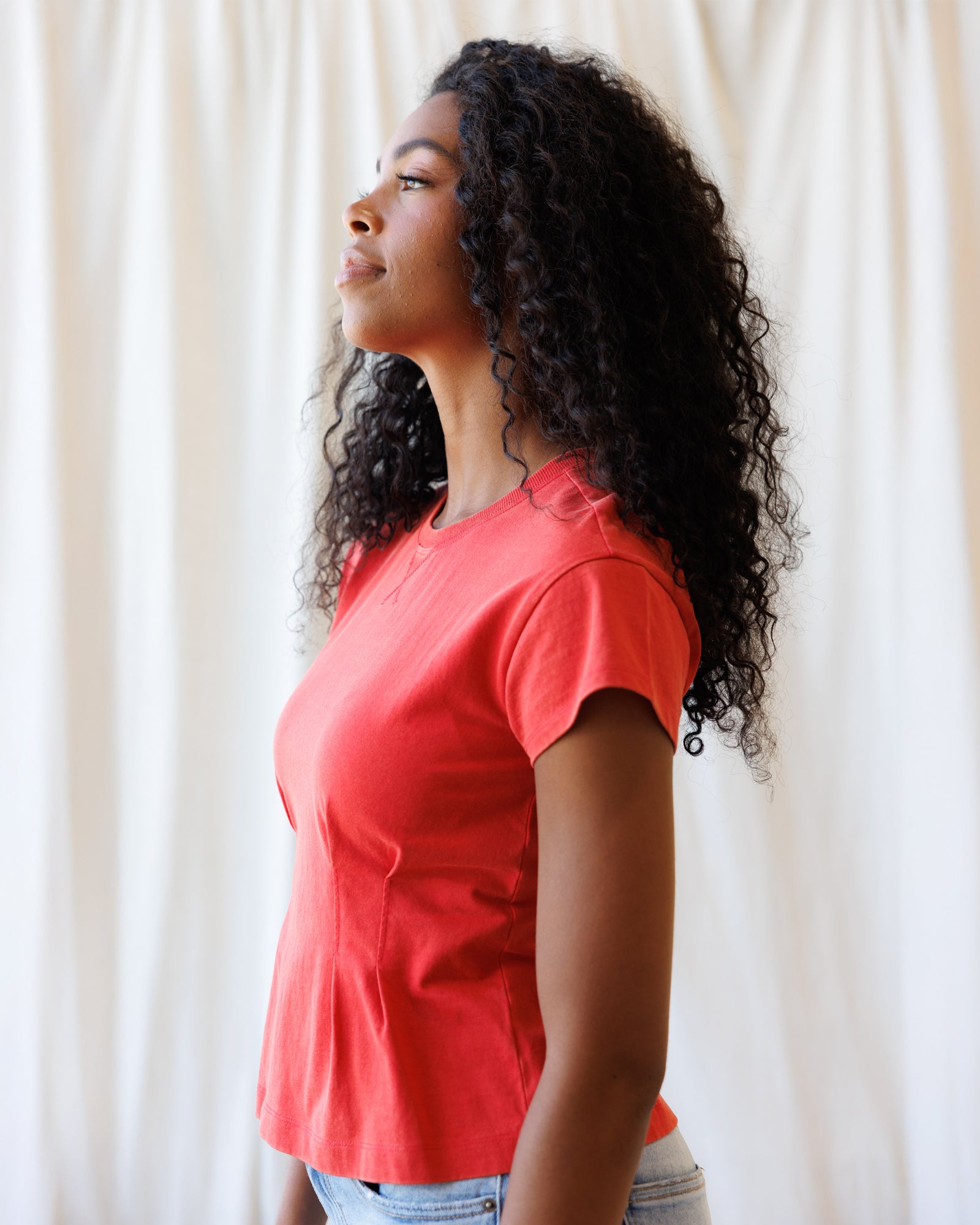 Woman wearing a red shirt against a white curtain background