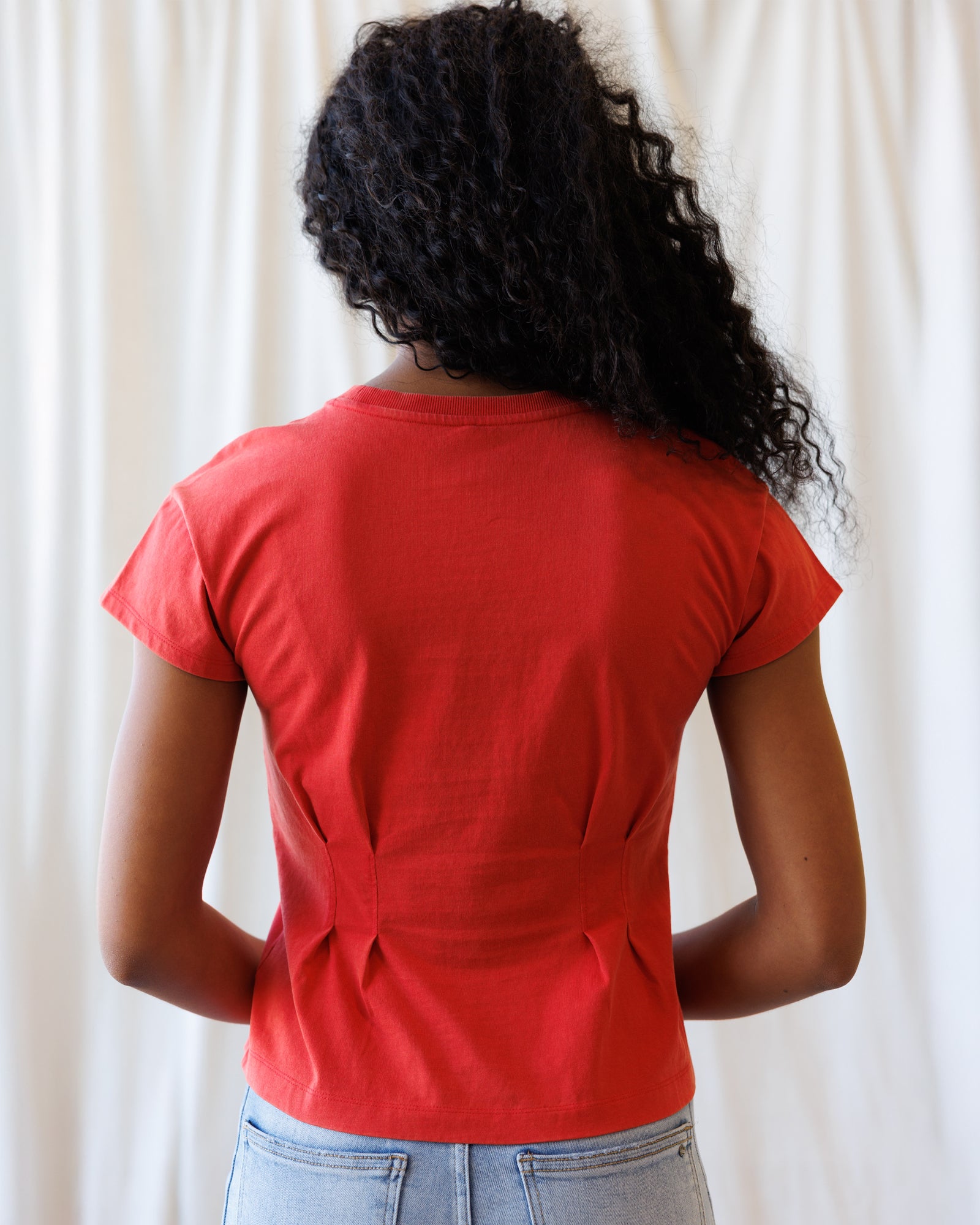 Person wearing a red t-shirt with a unique back design against a white curtain background