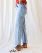 Person wearing light blue jeans and white sandals on a plain background