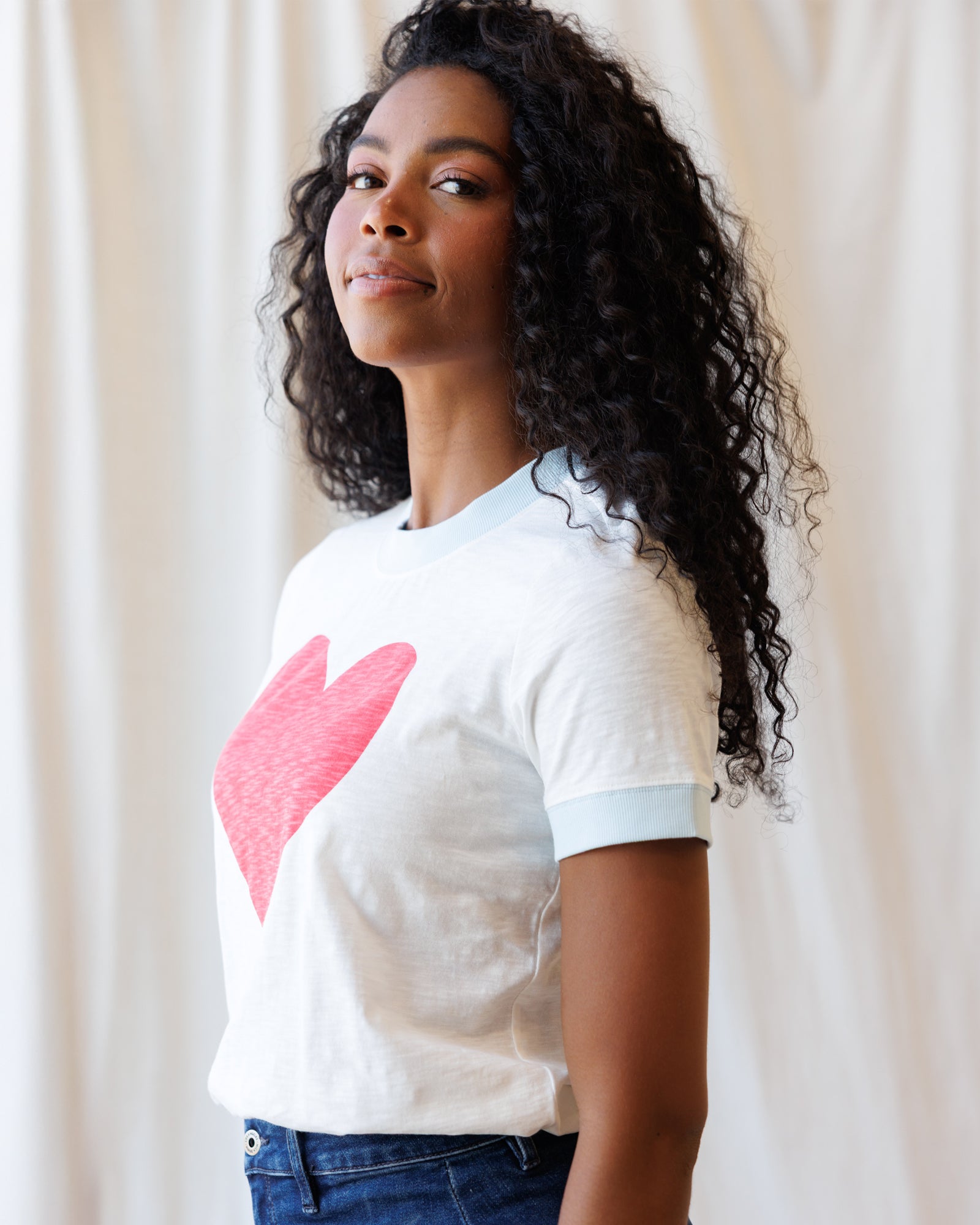 Woman wearing a white t-shirt with a pink heart design against a plain background