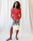 Woman wearing a red top and denim shorts holding a yellow bag against a white background