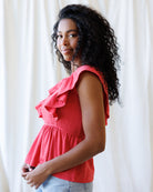 Woman wearing a coral ruffled top against a white curtain background