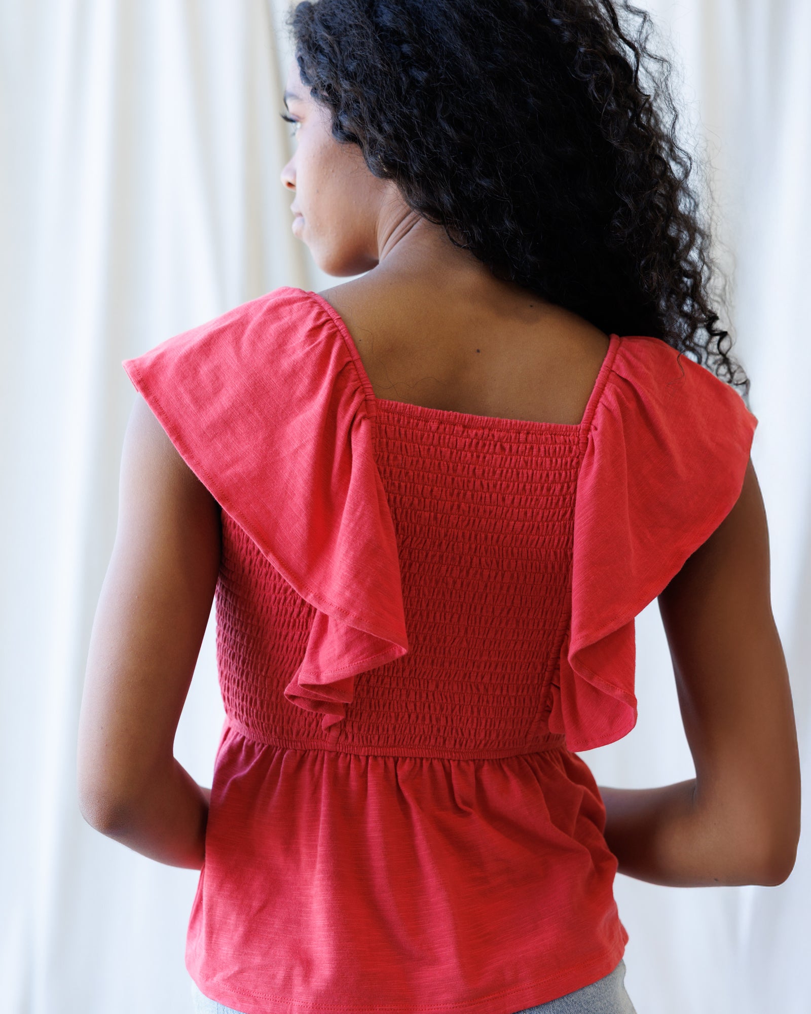 Woman wearing a red blouse with ruffled sleeves against a white curtain background