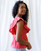 Woman wearing a pink blouse with ruffled sleeves against a white curtain background