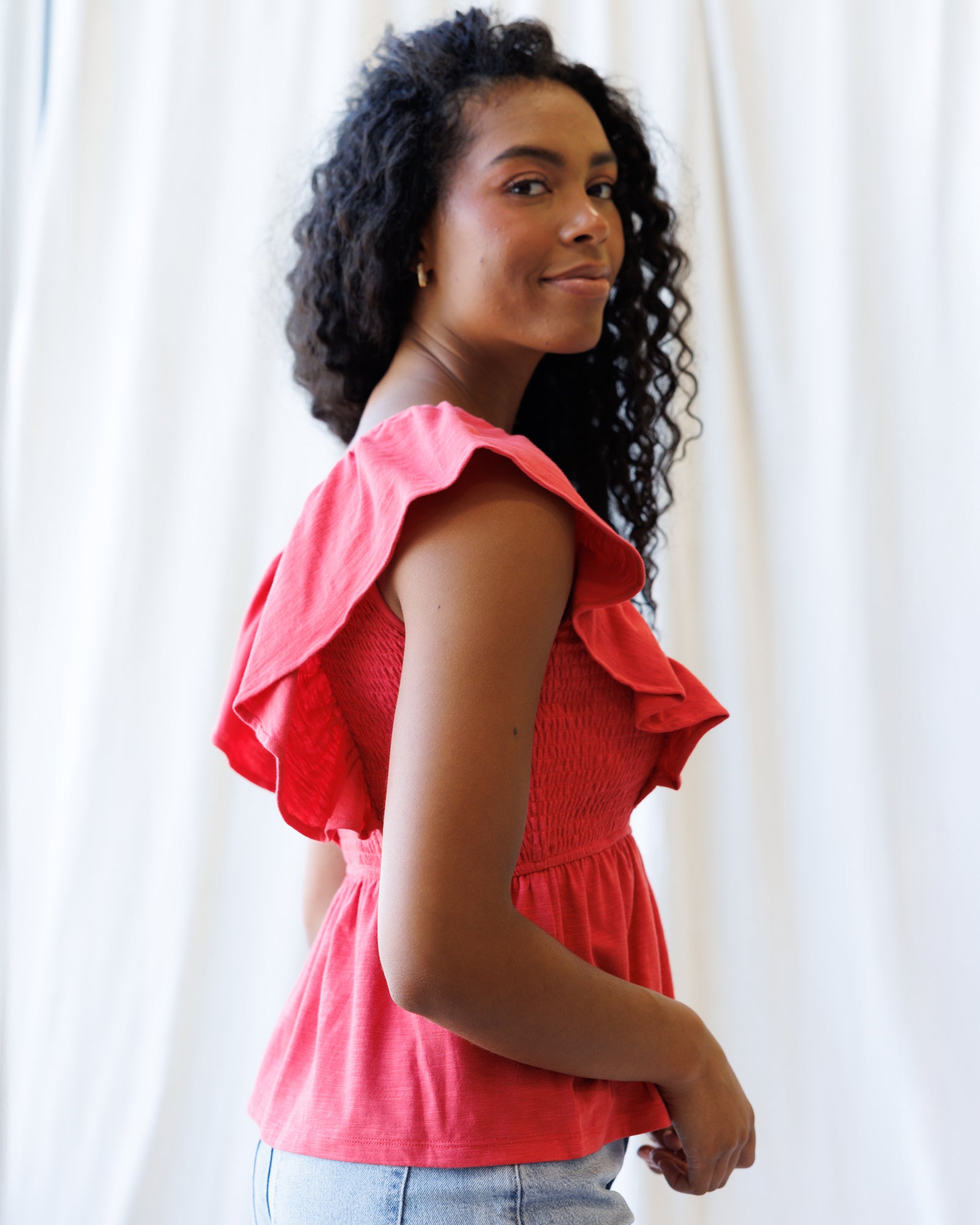 Woman wearing a pink blouse with ruffled sleeves against a white curtain background