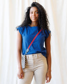 Woman wearing a blue top with a red strap over her shoulder against a white curtain background