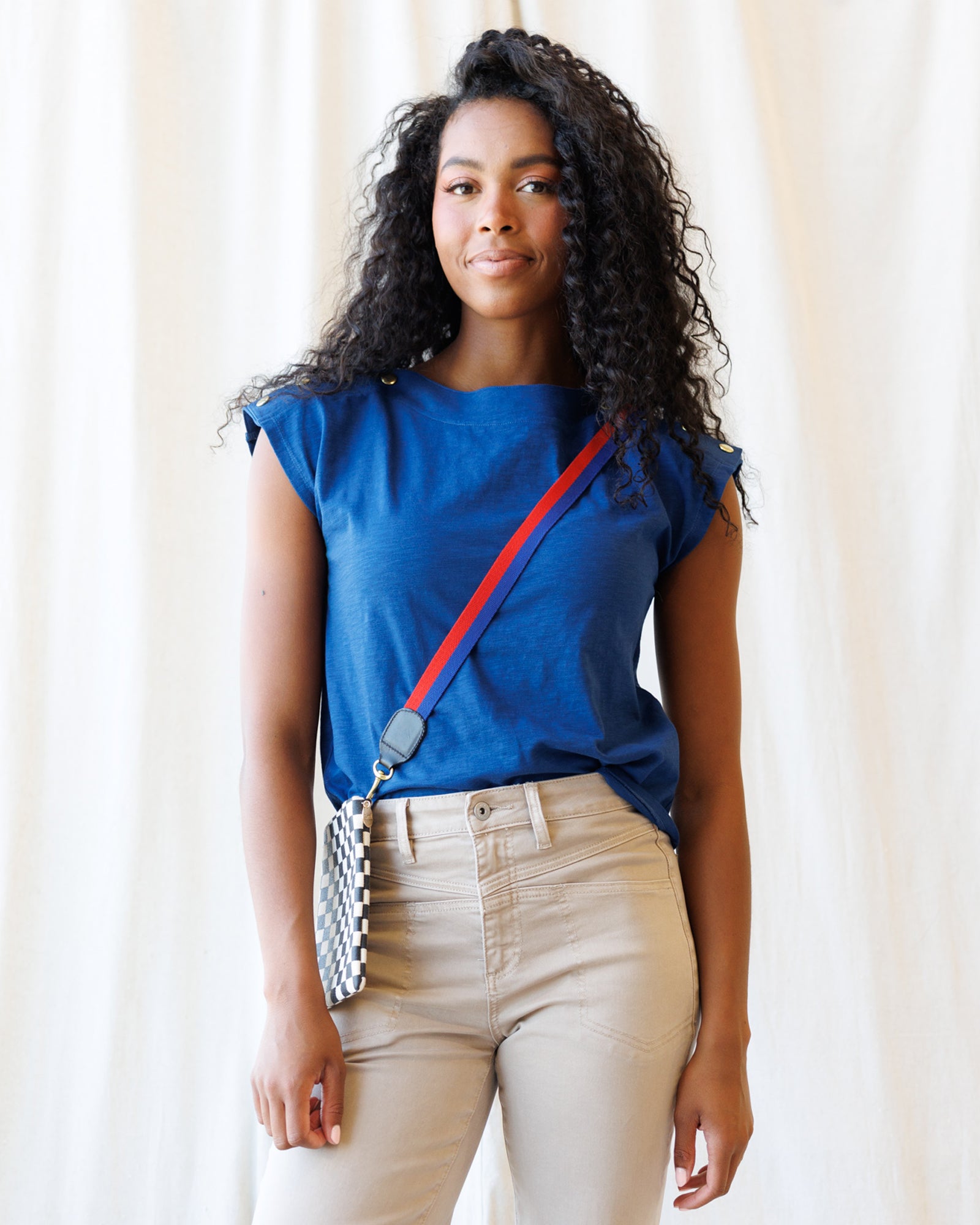 Woman wearing a blue top with a red strap over her shoulder against a white curtain background