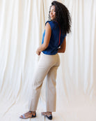 Woman wearing a blue top and beige pants against a white curtain background