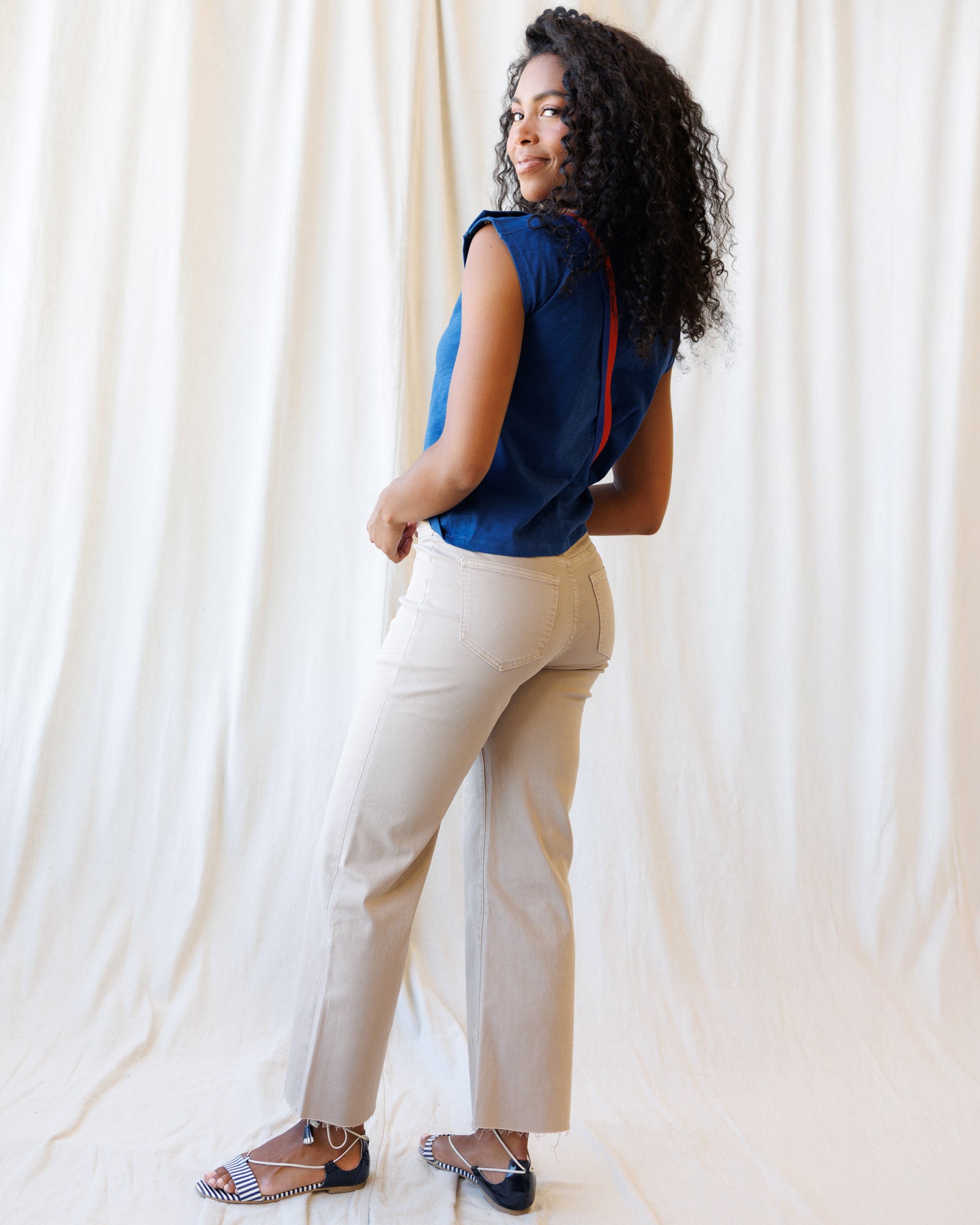 Woman wearing a blue top and beige pants against a white curtain background