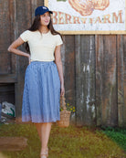 Woman in a checkered skirt and baseball cap standing in front of a berry farm sign.
