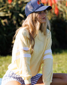 Woman wearing a yellow long-sleeve shirt and blue cap sitting outdoors.
