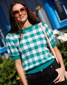 Woman wearing a green and white checkered sweater with sunglasses outdoors.