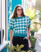 Woman wearing a green and white checkered shirt with sunglasses, standing outdoors.