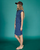 Woman wearing a blue denim dress and brown cap against a teal background