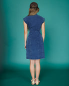 Woman wearing a blue denim dress against a teal background