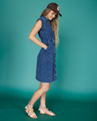 Woman wearing a blue denim dress and brown cap against a teal background