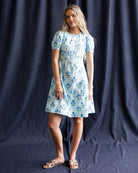 Woman wearing a light blue floral dress against a dark blue background