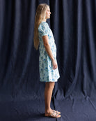 Woman wearing a floral dress standing against a dark blue curtain