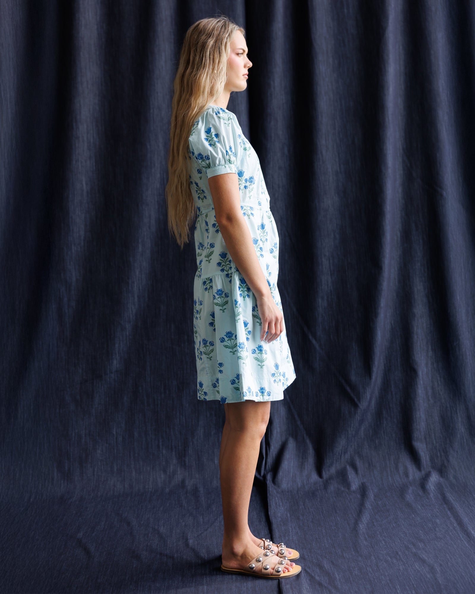 Woman wearing a floral dress standing against a dark blue curtain