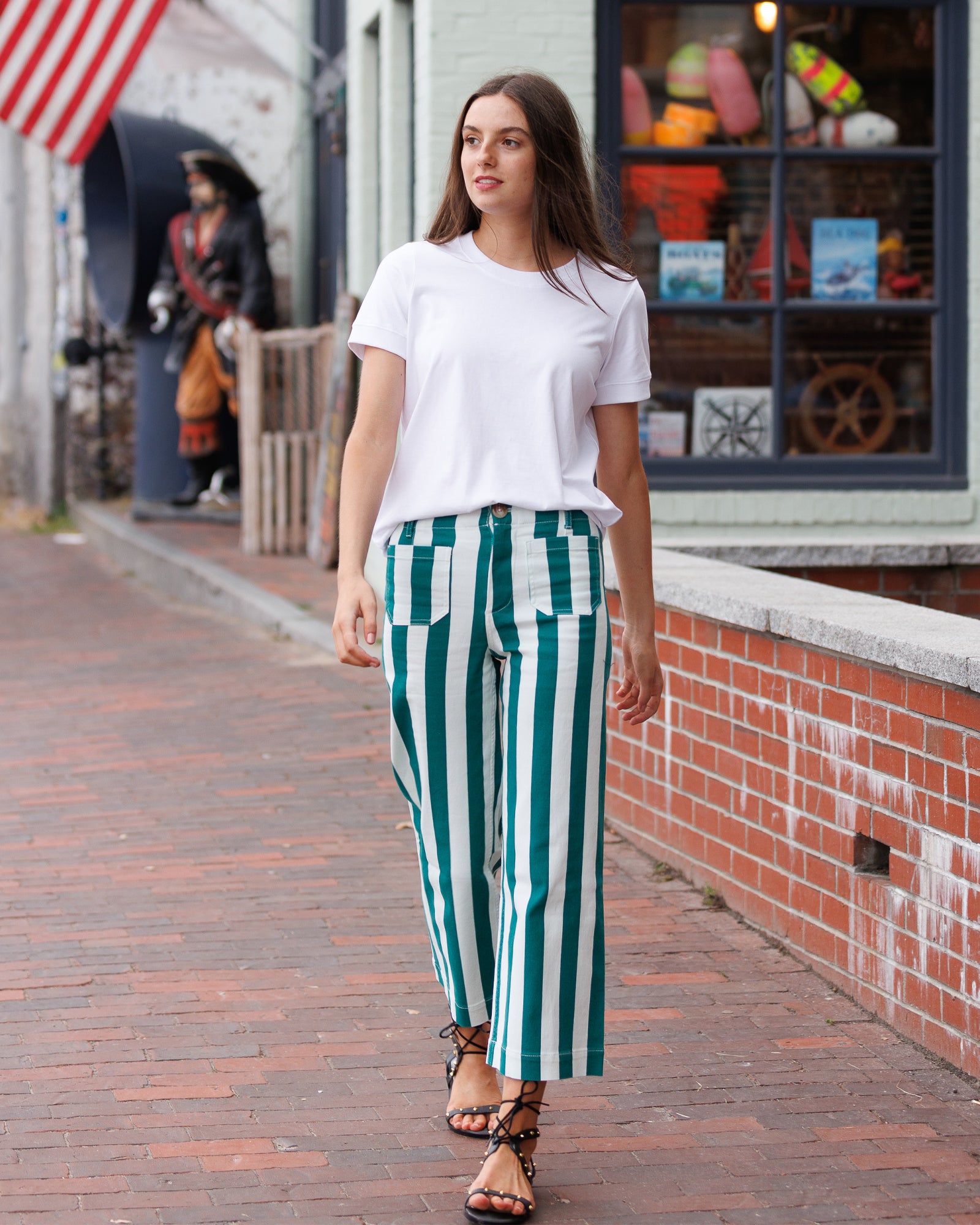 Woman wearing a white t-shirt and green striped pants walking on a sidewalk.