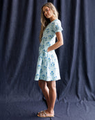 Woman wearing a light blue floral dress against a dark blue backdrop