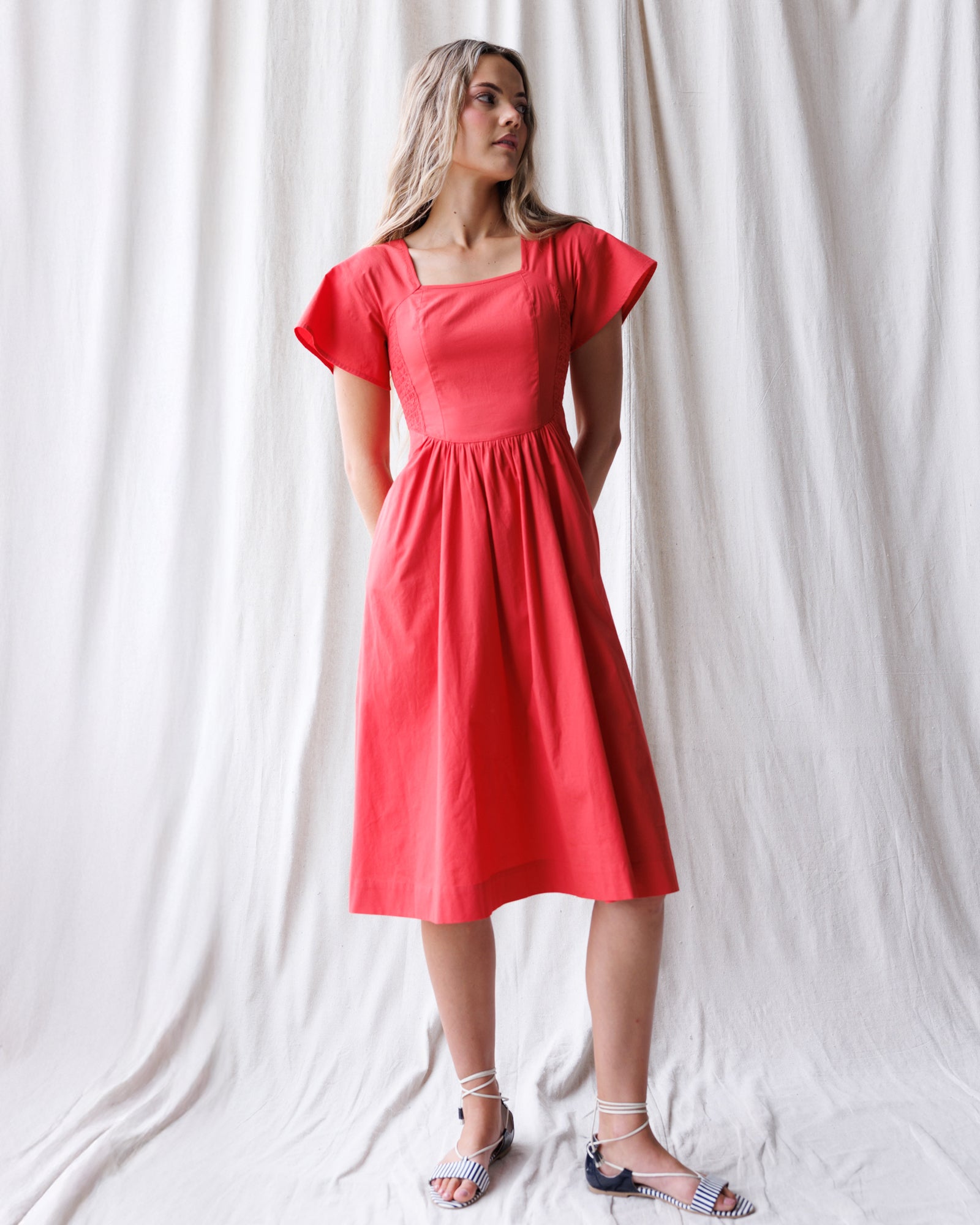 Woman wearing a red dress standing against a white curtain