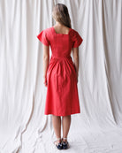 Woman wearing a red dress standing against a white curtain