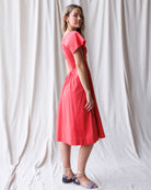 Woman wearing a red dress standing against a white curtain