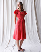 Woman wearing a red dress standing against a white curtain