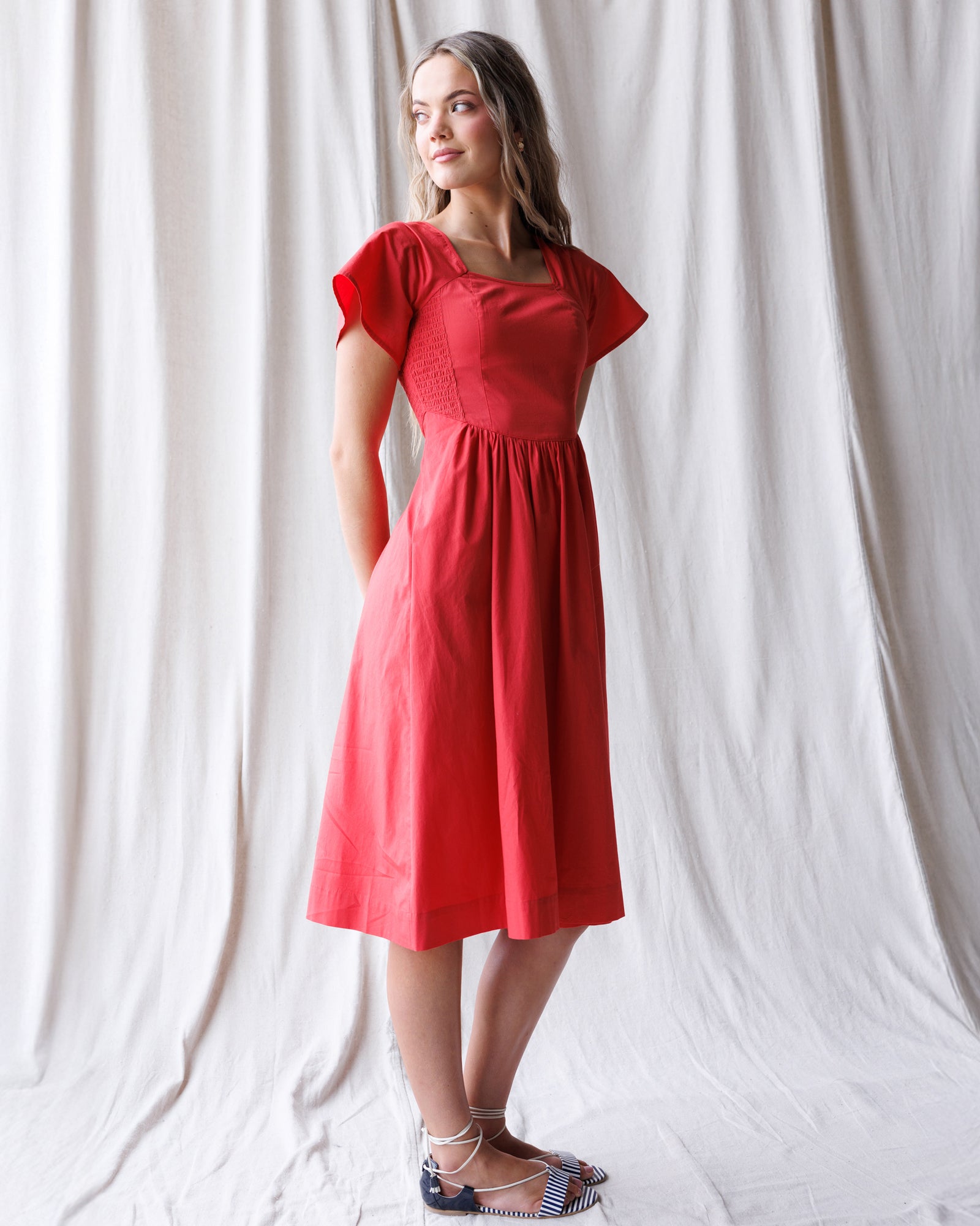 Woman wearing a red dress standing against a white curtain