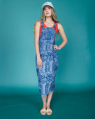 Woman wearing a blue patterned dress with red straps against a teal background