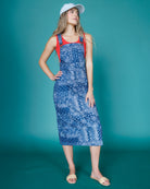 Woman wearing a blue patterned dress with red straps against a teal background