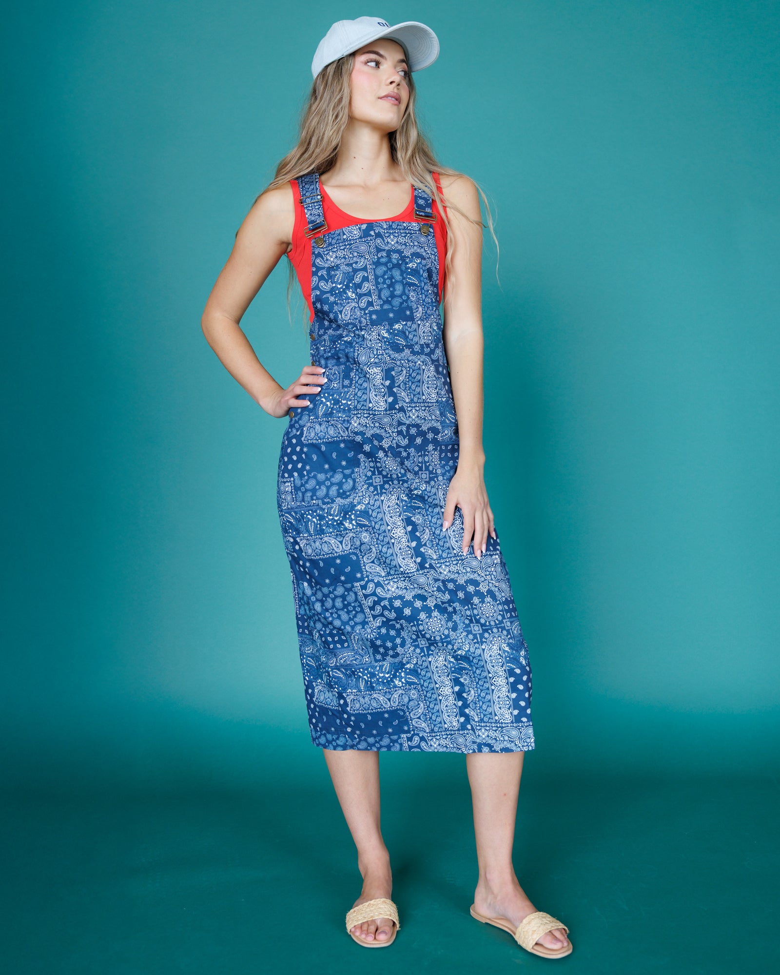 Woman wearing a blue patterned dress with red straps against a teal background