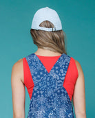 Woman wearing a blue patterned dress with a red top against a teal background