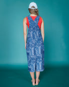 Woman wearing a blue patterned dress with a red top against a teal background