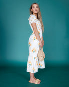 Woman wearing a white floral dress against a teal background