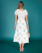 Woman wearing a white floral dress against a teal background
