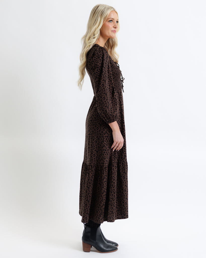 Woman wearing a long brown dress with a subtle pattern on a white background