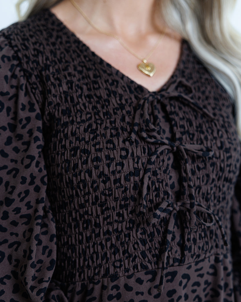 Brown blouse with black leopard print and a gold necklace with a heart pendant.