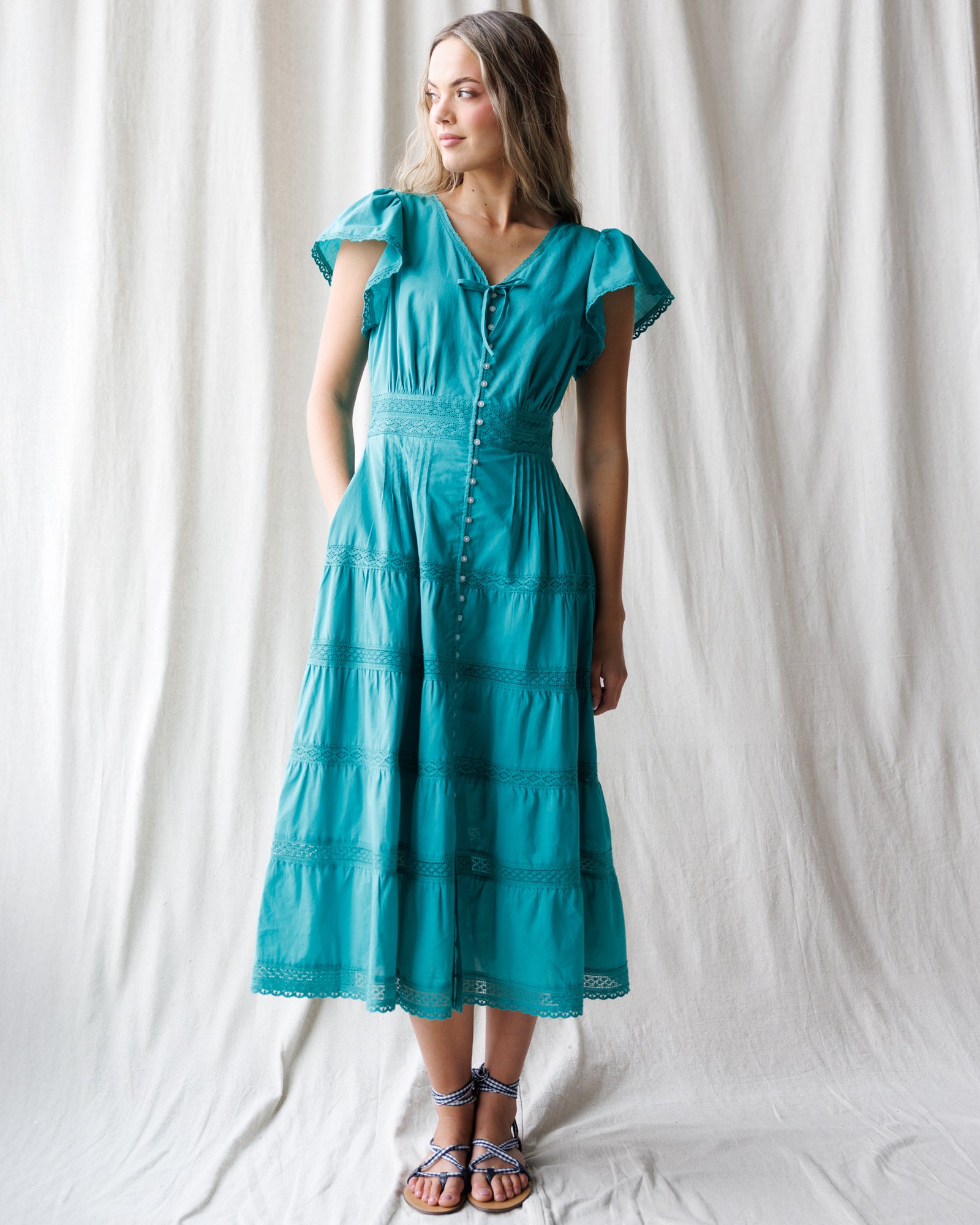 Woman wearing a teal dress against a white curtain background