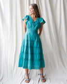 Woman wearing a teal dress against a white curtain background